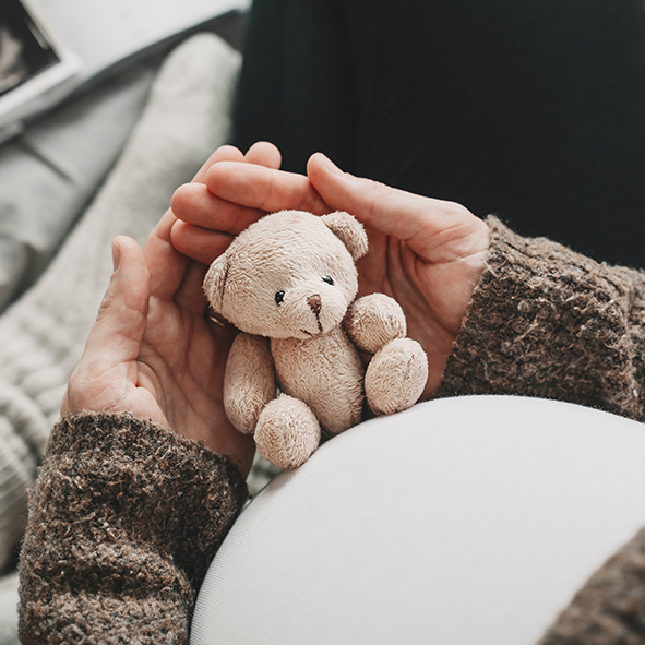 Pregnant woman holding small teddy bear.