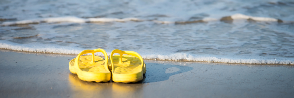 Picture of yellow sandals left on the beach with the ocean in the background.