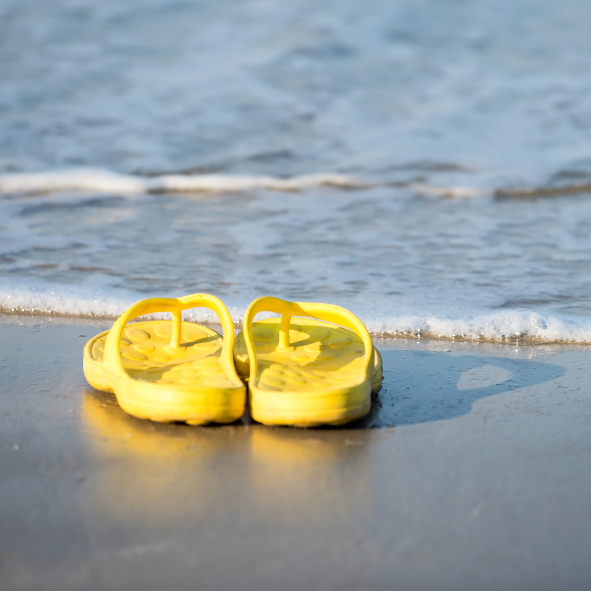 Picture of yellow sandals left on the beach with the ocean in the background.