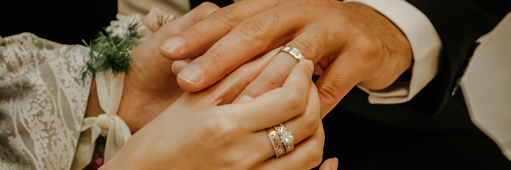 Close up picture of a couple's hands placing the wedding rings on their fingers.