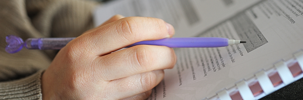 Picture showing a hand holding a pencil over a note book