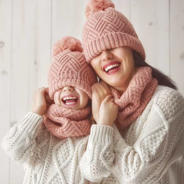 Picture of a mother and daughter wearing matching woollen jumpers, scarves, and hats.